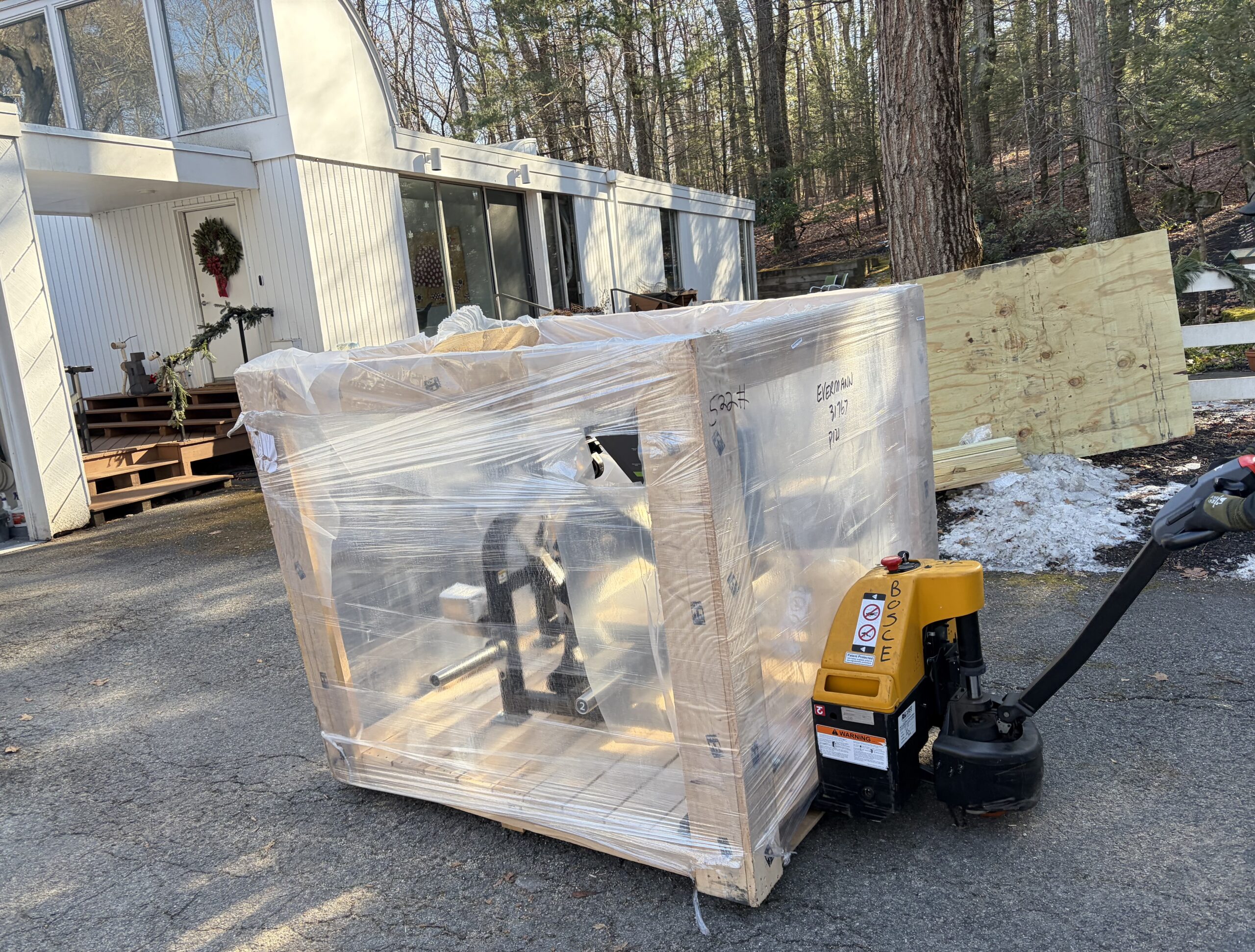 A crated PRIME Fitness leg extension and leg curl machine on a pallet jack in the driveway after delivery.