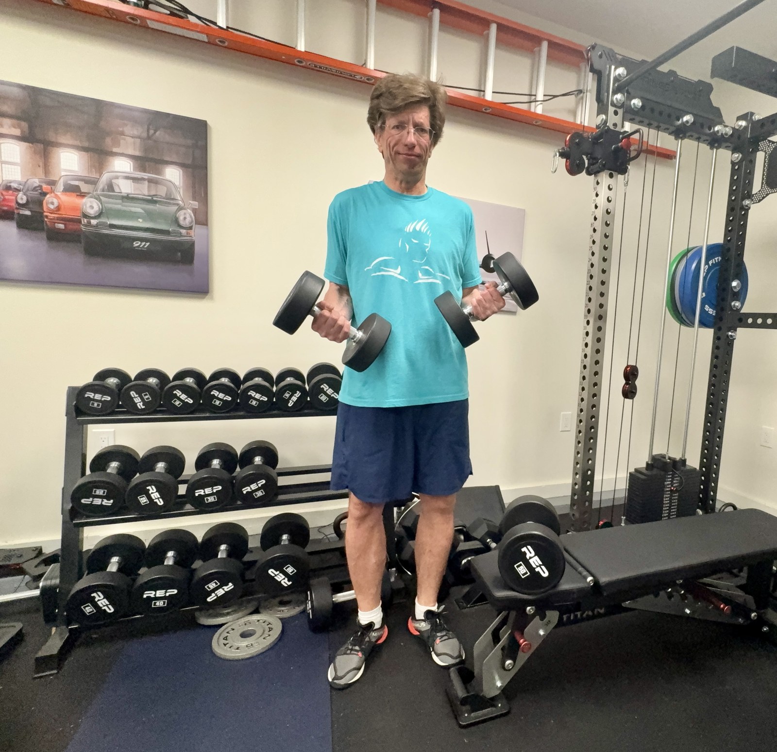 Gunnar, 53, holding two dumbbells in his garage gym with a loaded dumbbell rack and adjustable bench