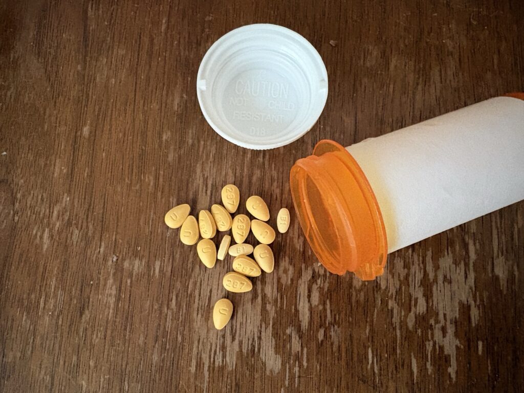 Yellow generic tadalafil 5 mg tablets, imprint 287, spilled from an amber prescription bottle on a wooden nightstand, the label turned away from the camera.