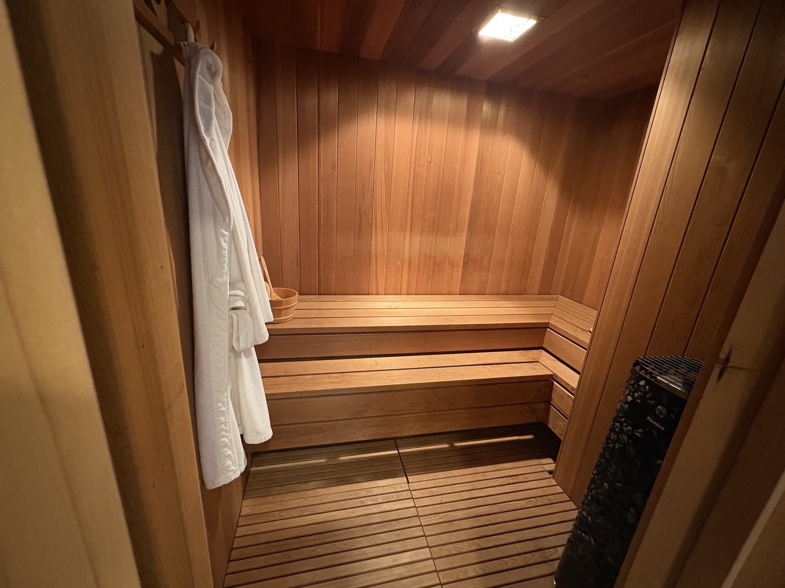 Interior of Gunnar's home sauna: cedar benches, a wooden bucket, and a robe hanging by the door.