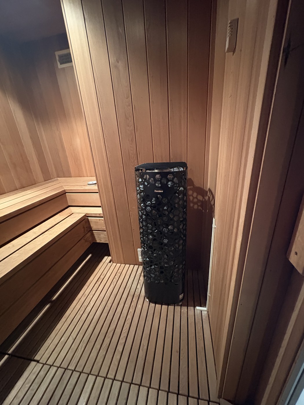 The Finnleo pillar heater in Gunnar's home sauna, black stone cage against cedar walls and a slatted floor.