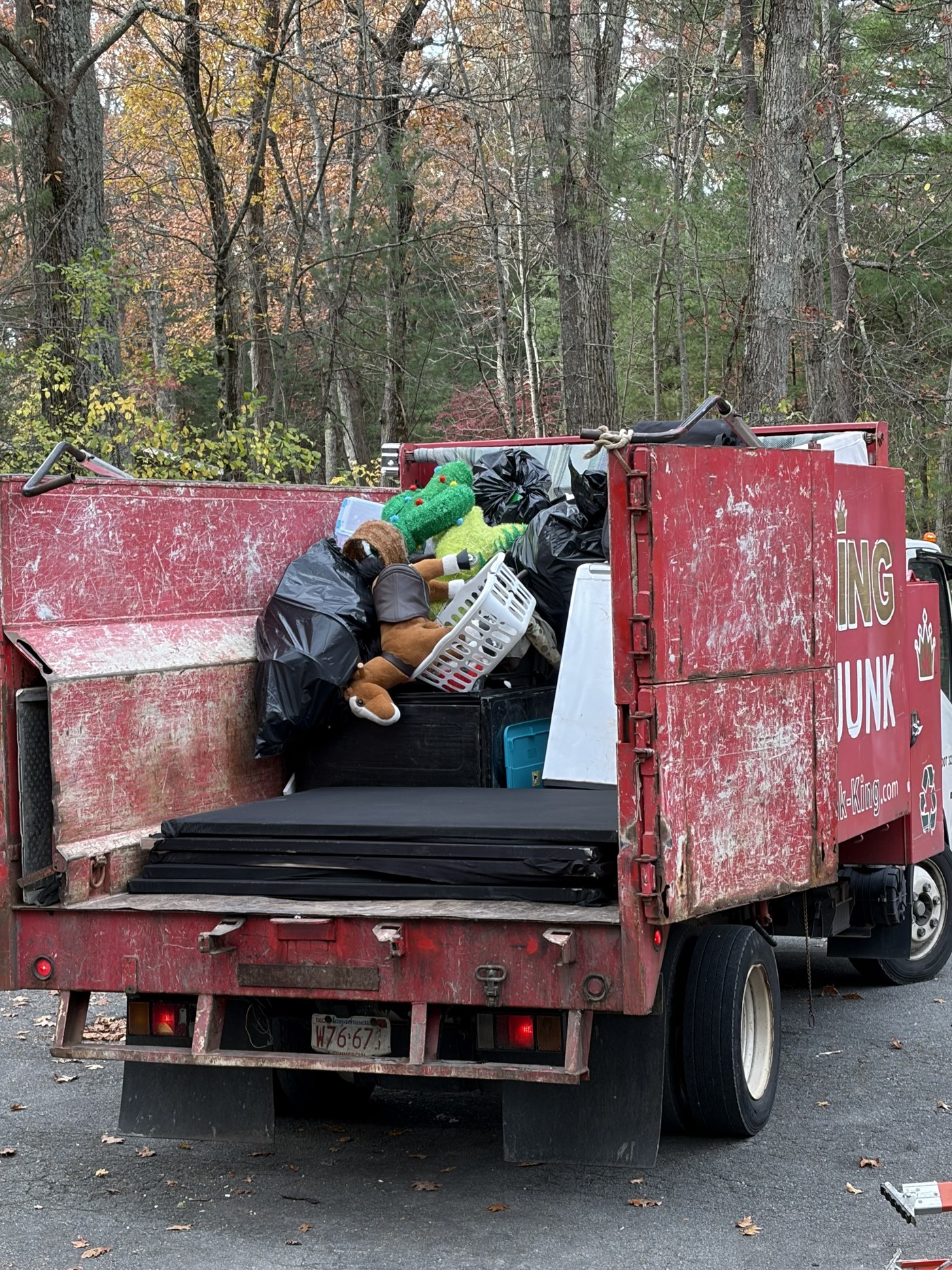 A junk removal truck in the driveway loaded with bagged junk and boxes cleared out of the garage.