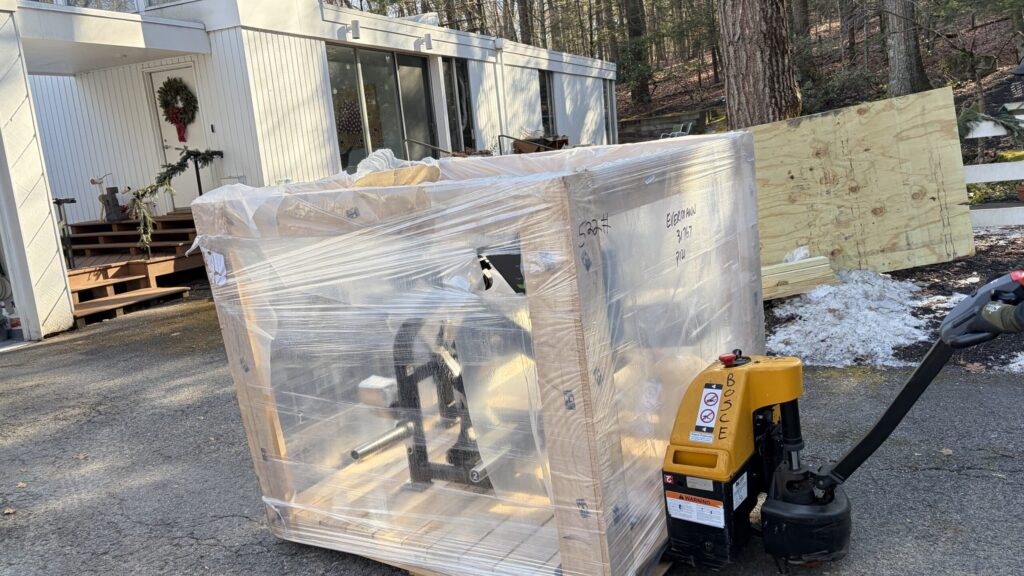 A crated PRIME Fitness leg extension and leg curl machine on a pallet jack in the driveway after delivery