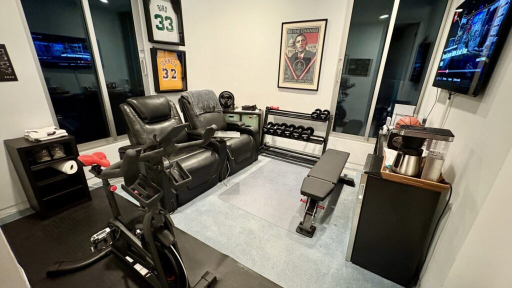 My home office set up for lifting: an indoor bike, an adjustable bench and a small rack of dumbbells in the corner